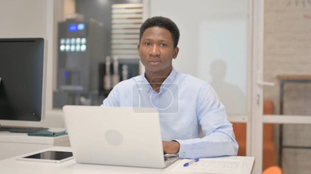 Photo for African Businessman Looking at Camera while Working on Laptop in Office - Royalty Free Image