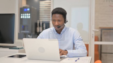 Photo for African Man with Headset Working on Laptop in Call Center - Royalty Free Image