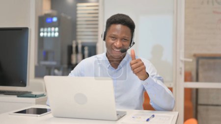 Photo for Thumbs Up by African Man with Headset Using Laptop in Call Center - Royalty Free Image