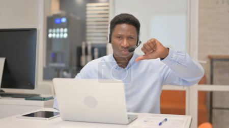 Téléchargez les photos : Pouces vers le bas par l'homme africain avec casque à l'aide d'un ordinateur portable dans le centre d'appels - en image libre de droit