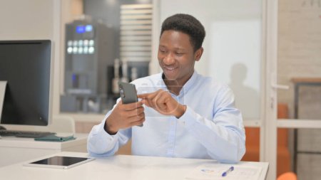 Photo for African Businessman Browsing Internet on Phone in Office - Royalty Free Image