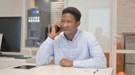Téléchargez les photos : Un homme d'affaires africain parle au téléphone au bureau - en image libre de droit