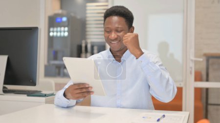 Foto de Empresario africano celebra éxito en tableta en oficina - Imagen libre de derechos