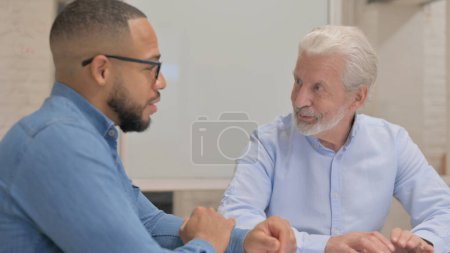Téléchargez les photos : Gros plan d'un vieil homme d'affaires parlant avec un homme de race mixte - en image libre de droit