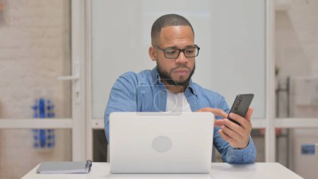 Téléchargez les photos : Homme de race mixte travaillant sur ordinateur portable et utilisant un smartphone - en image libre de droit