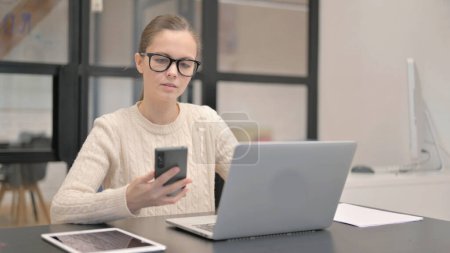 Téléchargez les photos : Jeune femme travaillant sur ordinateur portable et utilisant un smartphone - en image libre de droit