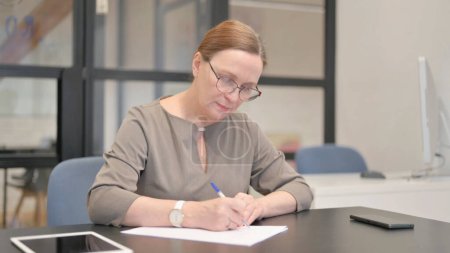 Téléchargez les photos : Ancienne femme d'affaires lisant des documents au travail - en image libre de droit
