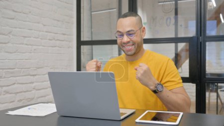 Photo for Excited Hispanic Man Celebrating Success on Laptop in Office - Royalty Free Image