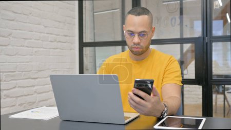 Photo for Hispanic Man Working on Laptop and Using Smartphone - Royalty Free Image
