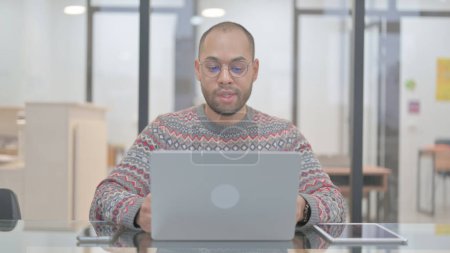 Foto de Hombre de raza mixta charlando en línea en el ordenador portátil mientras está sentado - Imagen libre de derechos