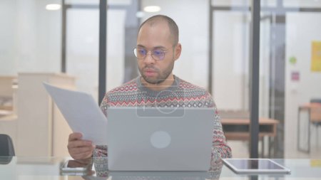 Téléchargez les photos : Homme de race mixte travaillant sur des documents et un ordinateur portable - en image libre de droit