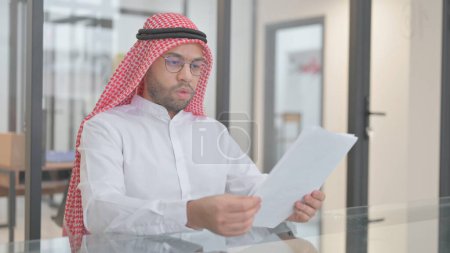 Téléchargez les photos : Jeune homme arabe lisant des documents au travail - en image libre de droit