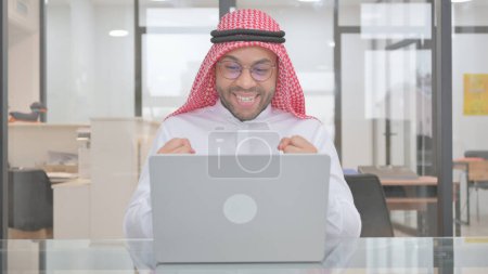 Téléchargez les photos : Jeune homme musulman célébrant le commerce en ligne sur ordinateur portable - en image libre de droit