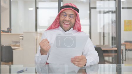 Téléchargez les photos : Jeune homme musulman célébrant en lisant des documents - en image libre de droit