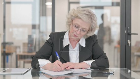 Téléchargez les photos : Femme d'affaires senior Rédaction d'un rapport d'entreprise au travail - en image libre de droit