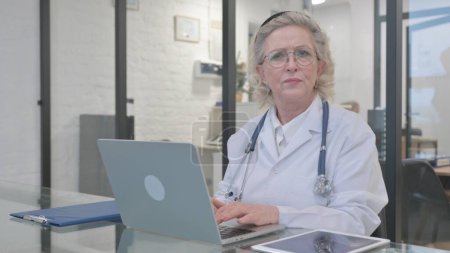 Old Lady Doctor Looking at Camera while Working in Clinic