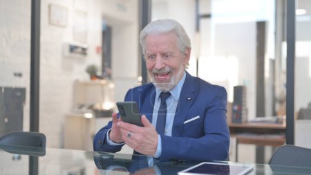 Téléchargez les photos : Un vieil homme d'affaires célèbre son succès au téléphone au bureau - en image libre de droit