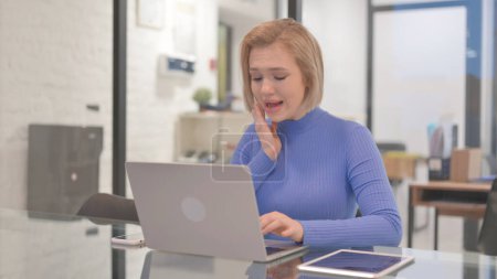 Téléchargez les photos : Jeune femme avec mal de dents travaillant sur ordinateur portable dans le bureau - en image libre de droit
