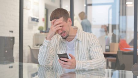 Photo for Creative Young Man Shocked by Loss on Phone in Office - Royalty Free Image