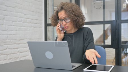 Téléchargez les photos : Angry Hispanic Woman Parler au téléphone au travail - en image libre de droit