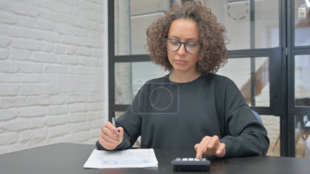 Téléchargez les photos : Femme hispanique faisant le calcul de la paperasserie au bureau - en image libre de droit