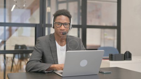 Foto de Hombre afroamericano con auriculares mirando a la cámara mientras trabaja en el ordenador portátil - Imagen libre de derechos