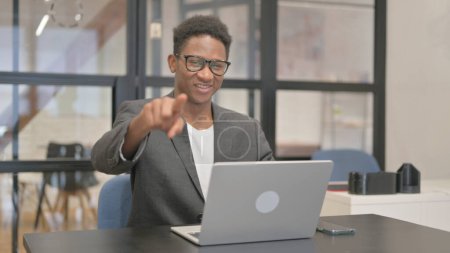 Téléchargez les photos : Afro-Américain pointant vers la caméra tout en travaillant sur ordinateur portable - en image libre de droit