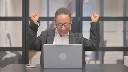 Téléchargez les photos : Femme d'affaires mixte excitée pour le trading en ligne sur un ordinateur portable au bureau - en image libre de droit