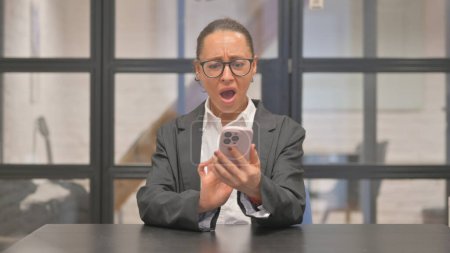 Photo for Mixed Race Business Woman Shocked by Online Trading Loss on Phone in Office - Royalty Free Image