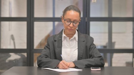 Téléchargez les photos : Femme d'affaires métisse écrivant une lettre au travail - en image libre de droit