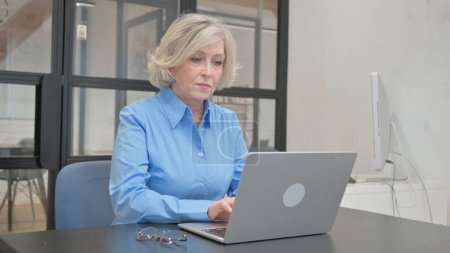 Téléchargez les photos : Vieille femme âgée travaillant sur ordinateur portable au bureau - en image libre de droit