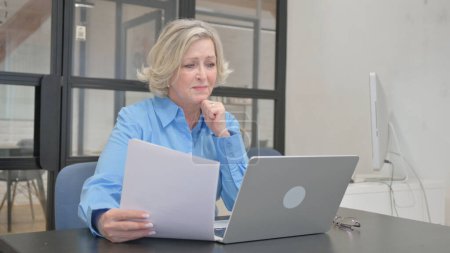 Foto de Mujer mayor tensa sintiéndose molesta por el trabajo en el ordenador portátil y los documentos - Imagen libre de derechos