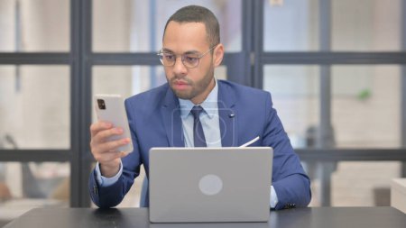Téléchargez les photos : Homme d'affaires de race mixte utilisant le téléphone avec ordinateur portable - en image libre de droit