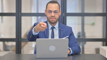 Téléchargez les photos : Mixte Race Homme d'affaires pointant vers la caméra tout en travaillant sur ordinateur portable - en image libre de droit