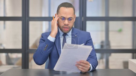 Téléchargez les photos : Mixte Race Homme d'affaires se sentant bouleversé tout en lisant contrat - en image libre de droit