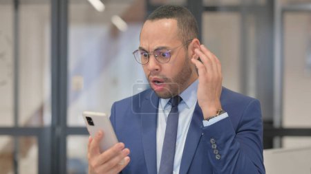 Téléchargez les photos : Portrait d'un homme d'affaires de race mixte choqué par une perte au téléphone - en image libre de droit