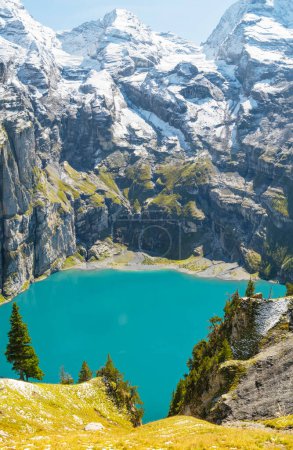 Photo for Oeschinensee lake with snow Bluemlisalp mountain on sunny summer day. Panorama of the azure lake Oeschinensee, pine forest in Swiss alps, Kandersteg. Switzerland. - Royalty Free Image