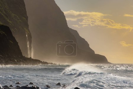 Foto de Acantilados de roca volcánica Achadas da Cruz en luz solar retroiluminada. Olas del Océano Atlántico. Hermoso paisaje marino al atardecer de la isla turística de Madeira, Portugal - Imagen libre de derechos