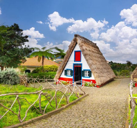 Foto de Casas de cabañas tradicionales y jardín de Madeira en el pueblo Santana. Día soleado en Portugal, destino turístico - Imagen libre de derechos