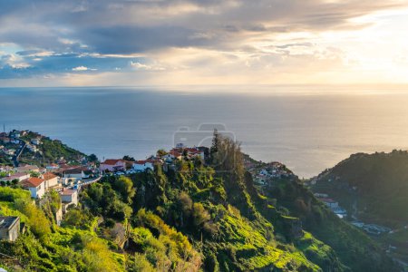 Foto de Casas Tadicionales Madeiran en Funchal detrás de una plantación de plátanos y puesta de sol en el océano. - Imagen libre de derechos