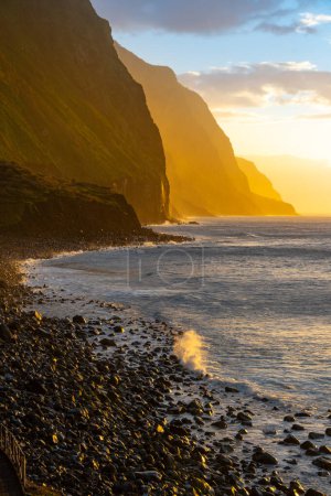 Foto de Acantilados de roca volcánica Achadas da Cruz en luz solar retroiluminada. Olas del Océano Atlántico. Hermoso paisaje marino al atardecer de la isla turística de Madeira, Portugal - Imagen libre de derechos