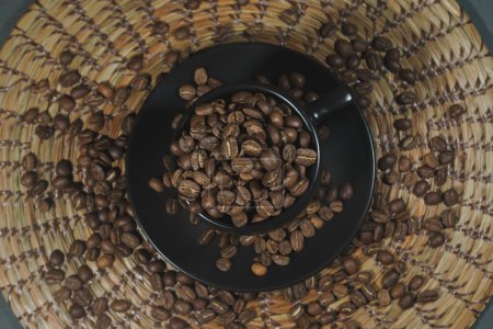 Foto de Vista área de taza negra llena de granos de caf sobre tapete artesanal tejido, artesana y granos de caf tostado - Imagen libre de derechos