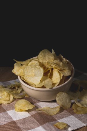 Photo for Potato chips in a beige bowl on a table full of crispy potato chips - Royalty Free Image
