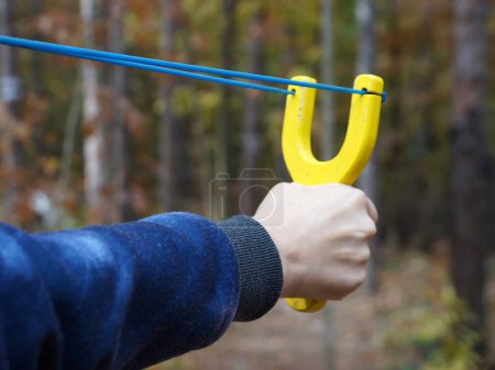 Téléchargez les photos : Fronde avec une corde à arc tendue dans une main féminine sur fond de plan rapproché d'une forêt - en image libre de droit
