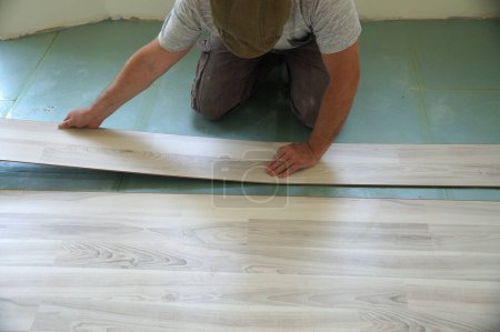 Téléchargez les photos : Travailleur pose stratifié plancher dans une pièce. - en image libre de droit