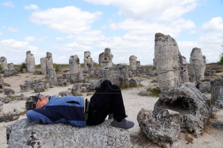Foto de Un turista solitario descansa sobre una piedra en un museo histórico al aire libre entre antiguos pilares de piedra. - Imagen libre de derechos