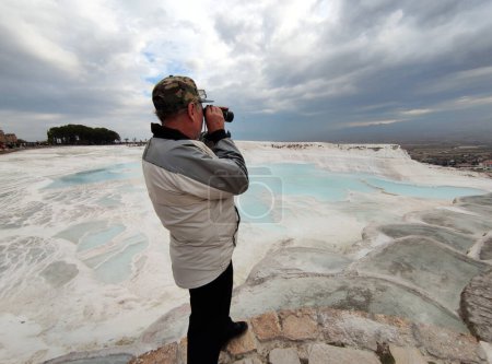 A man looking through a spotting scope from above at the panorama of Pamukkale, Turkey.