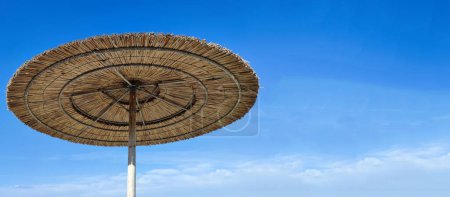 Straw beach umbrella against blue sky, copy space