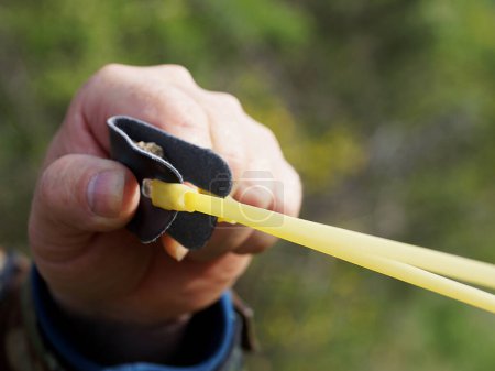 A man pulls the rubber band of a slingshot for a shot in the forest close-up
