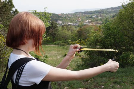 A teenage girl aims a slingshot for a shot in the forest.